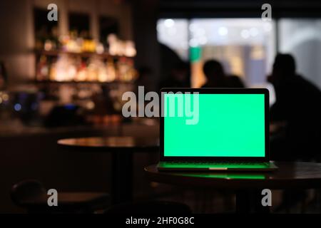 green screen laptop computer on bar table at night. Stock Photo