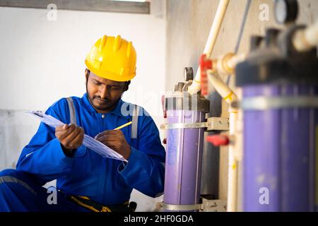 young indian plumber or repairman noting water level at under construction building - concept of professional occupation, and maintenance service. Stock Photo