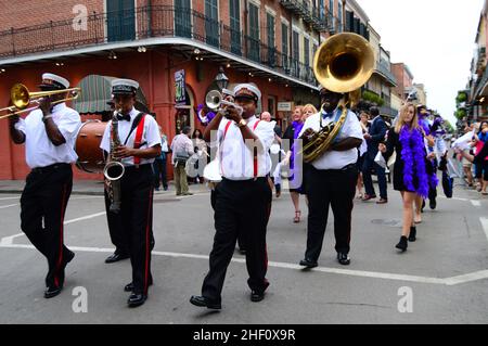 A second line brass jazz band parades down Bourbon Street in the French Quarter of New Orleans while party goers march and dance behind them Stock Photo