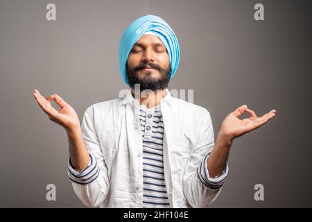 young indian sikh man relaxing by doing zen meditation on grey background - concept of relaxation, healthy lifestyle and leisure activities. Stock Photo