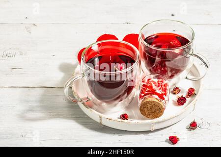 Hibiscus tea. The healthy hot organic drink is served in glass cups. St.Valentine's symbols as hearts, rose petals, and sweet sugar candies. Hard ligh Stock Photo