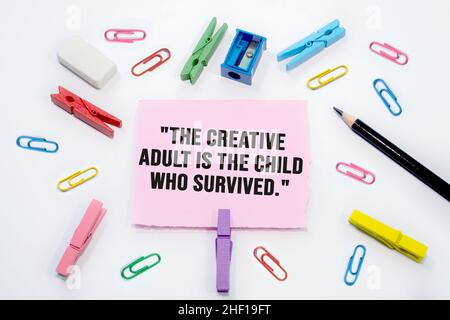 Text sign showing The creative adult is the child that has survived on Set of colorful paper clips with white copy space background. Stock Photo