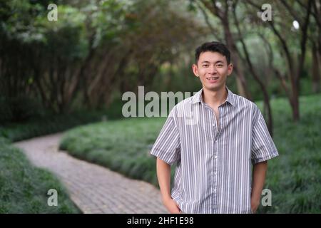 one Asian young man smiling and looking at camera in natural green park Stock Photo