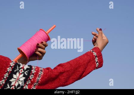 Female holding Kite phirki Manjha or kite spool thread reel in hand and flying kite at house celebrating Indian kite festival of Makar sankranti or Ut Stock Photo