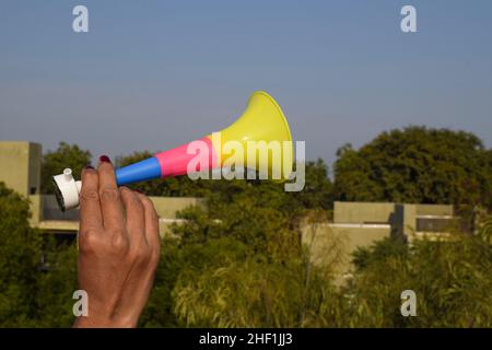 Person holding Trumpet shaped whistle blowing horn known as Pipudi or pipudo in gujarati. Blown during kite festival of Uttarayan or Makar sankranti i Stock Photo
