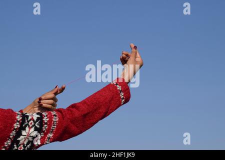 Female holding Kite phirki Manjha or kite spool thread reel in hand and flying kite at house celebrating Indian kite festival of Makar sankranti or Ut Stock Photo