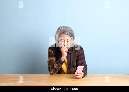 The senior Asian man using smart phone at the working desk with blue background. Stock Photo