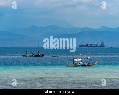 Sarangani Bay with two tuna fishing boats moored at the village of Tinoto, Maasim in the foreground. In the background, there is a container ship on i Stock Photo