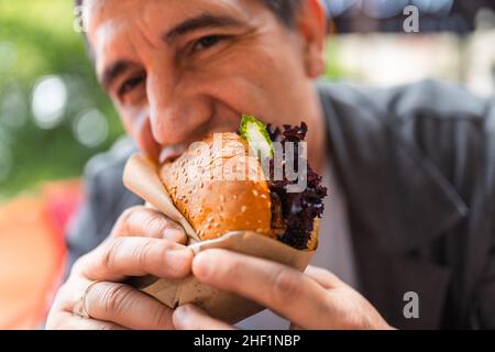 man with greed and appetite eats burger in fast food restaurant and enjoys delicious meal Stock Photo