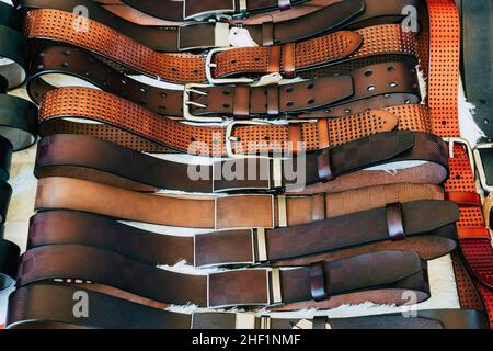 Various types of brown leather belt in a row for display and sale on the market. Realistic leather belts set with metal buckles. Clothing store, shelf Stock Photo
