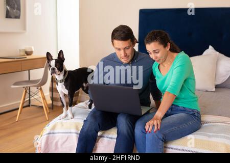 Caucasian couple using laptop sitting together on the bed at home Stock Photo