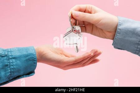 Owner gives the tenant the keys with a keychain from the house. Close up of females hands. Pink background. The concept of mortgages, rental of real e Stock Photo