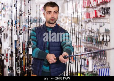 active man choosing fishing rod for fishing in the sports shop Stock Photo
