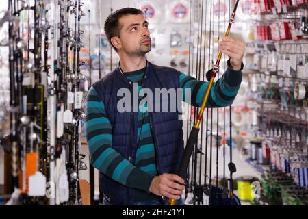 interested man choosing fishing rod for fishing in the sports shop Stock Photo