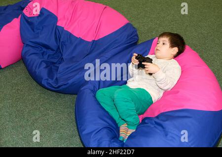 A handsome boy of 4 years old plays a game console, holds a joystick in his hands and looks away, a place for text Stock Photo