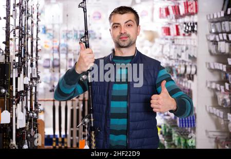 satisfied man choosing fishing rod for fishing in the sports shop Stock Photo