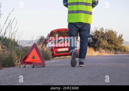 Man with his back to the camera puts a warning triangle behind his car Stock Photo