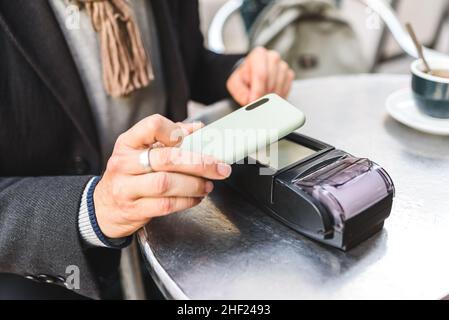 High angle of unrecognizable male client using smartphone with NFC chip to pay for order while sitting at cafeteria table Stock Photo