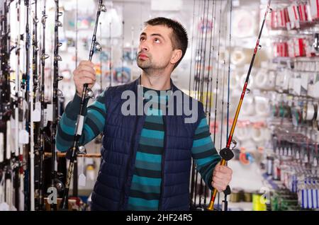 serious man choosing fishing rod for fishing in the sports shop Stock Photo