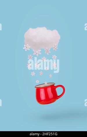 Creative concept with cloud, falling winter snowflake and red mug on patel blue background. Minimal winter holidays concept. Stock Photo