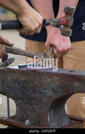 Farrier making nail holes on a horse shoe, on an anvil.   Patron saint of blacksmiths is St Eligius. Stock Photo