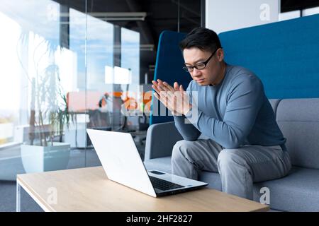 Pensive asian man working from office sitting at desk, making important decision, serious and focused businessman Stock Photo