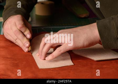 Shoemaker hands cutting terracotta suede leather in workshop. Closeup Stock Photo