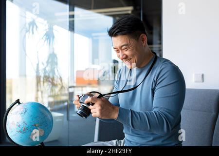 Portrait of an Asian photographer, happy male tourist blogger, working in home office, blogs about travel and teaches photography Stock Photo