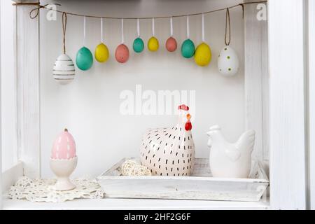 Fragment of the interior. Decorated children's room for Easter. A garland of plastic eggs on the wall. Ceramic hens on the tray on the table. Place fo Stock Photo