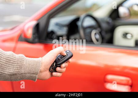 Male hand holding electronic remote key pushing button near red rental car Stock Photo
