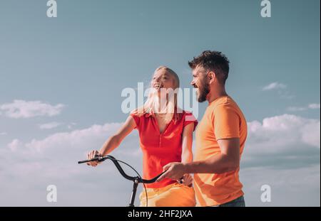Summer woman with retro bike on blue sky background. Happy loving couple. Greatest Love Stories. Couple in summer dress rides a bike. Couple with Stock Photo