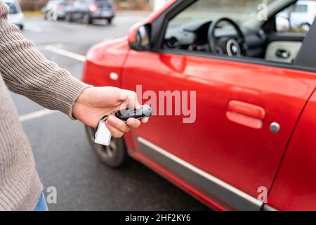 Male hand holding electronic remote key pushing button near red rental car Stock Photo