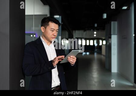 Serious asian male worker focused on work working with tablet computer in modern office Stock Photo