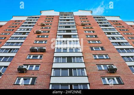 Wall of modern brick residential building with windows and balconies against blue sky. High residential building. Stock Photo