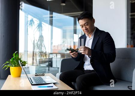Asian boss businessman makes online shopping sitting in the office, thoughtful makes a choice in the online store Stock Photo