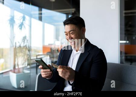 Happy asian man shopping online, businessman in office, shopping in online store using credit card, happy with the loan Stock Photo