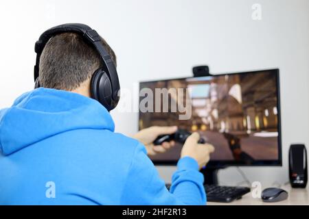 Man in headphones playing with a gamepad a computer game on desktop PC. Concept of game addiction, home leisure Stock Photo