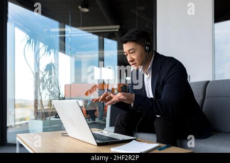 Asian call center employee talking to customers sitting in office, Asian businessman using headset and laptop for video call happy and smiling Stock Photo