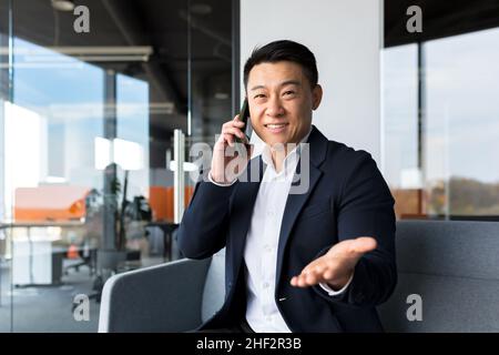 Successful Chinese Asian businessman looks at the camera and smiles talking on the phone Stock Photo