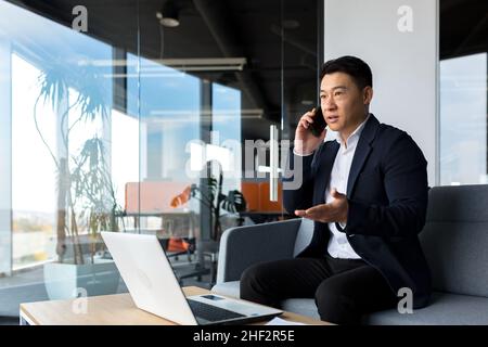 Thinking asian businessman businessman, talking on the phone working in a modern office, listening seriously Stock Photo