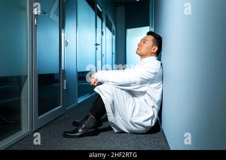 Upset and thinking asian man sitting on the floor in the laboratory, frustrated scientist Stock Photo