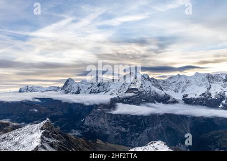 View of the famous peaks Jungfrau, Mönch and Eiger from the mountain Schilthorn in the Swiss Alps Switzerland at sunrise with dramatic clouds and snow Stock Photo