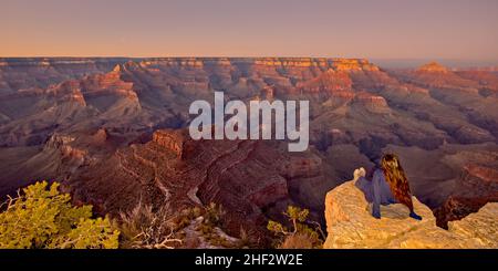A young woman sitting on the edge of a cliff looking out at the vastness of the Grand Canyon from Shoshone Point at twilight. The woman is facing away Stock Photo