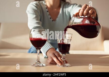 Woman pouring freshly squeezed red beet juice into two glasses indoors in sunlight Stock Photo