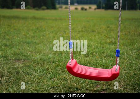 Small plastic kid hanging swing, blurred meadow in background Stock Photo