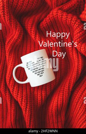 A white cup with a heart stands on a red knitted fabric. Inscription of St. Valentine's day, 14 February Stock Photo