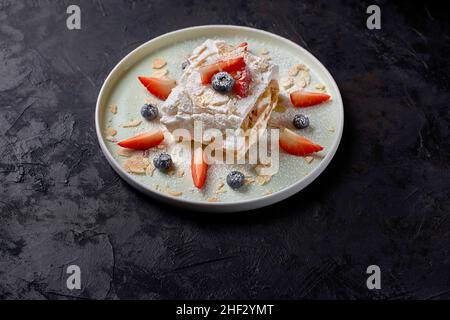 meringue roll with strawberries, blueberries, raspberries and cranberries. Dessert decorated with fresh berries on a black table. Stock Photo