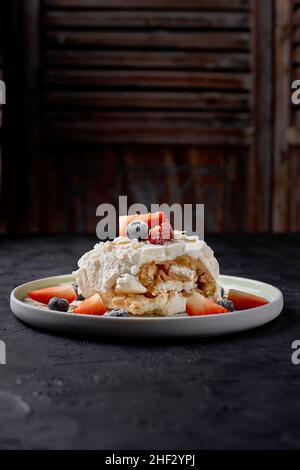 meringue roll with strawberries, blueberries, raspberries and cranberries. Dessert decorated with fresh berries on a black table. Stock Photo