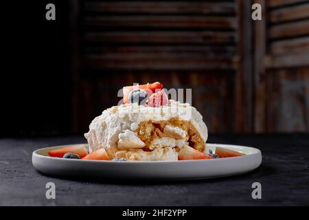 meringue roll with strawberries, blueberries, raspberries and cranberries. Dessert decorated with fresh berries on a black table. Stock Photo