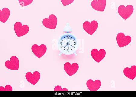 Valentines Day background with small white alarm clock and red hearts on pink. Love, dating, dinner planning and shopping gifts concept. Top view Stock Photo